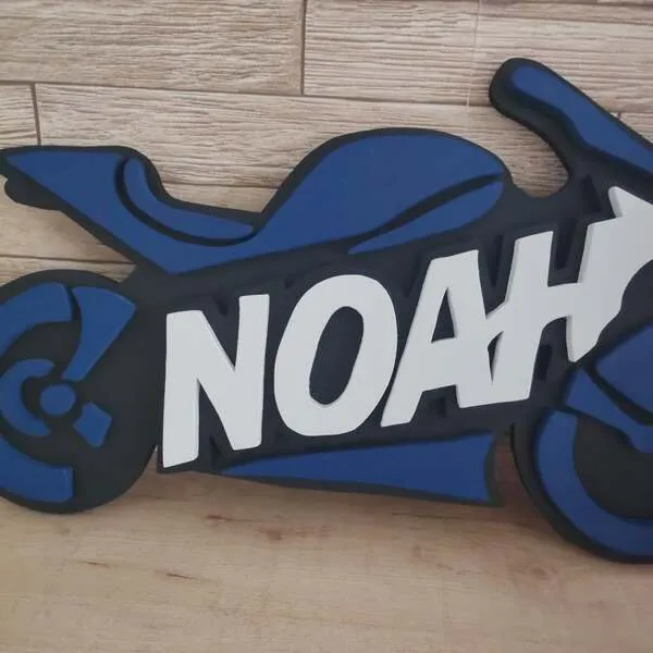 Gros plan sur une plaque de porte moto personnalisée Noah en bois, avec lettres blanches en relief et carrosserie bleue et noire.