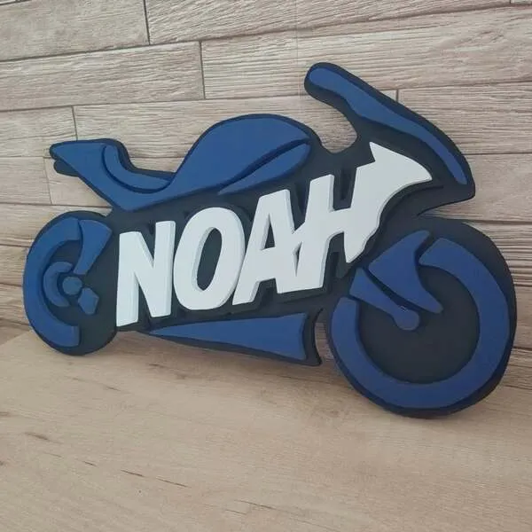 Plaque de porte moto personnalisée Noah en bois peint bleu et noir, avec prénom blanc en relief, décoration artisanale pour chambre d’enfant.