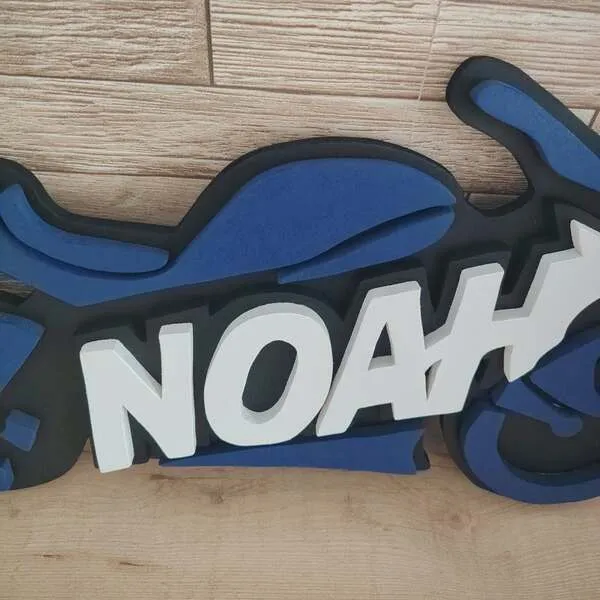 Gros plan sur le prénom Noah en lettres blanches en relief, intégré à une plaque de porte moto personnalisée en bois bleu et noir.