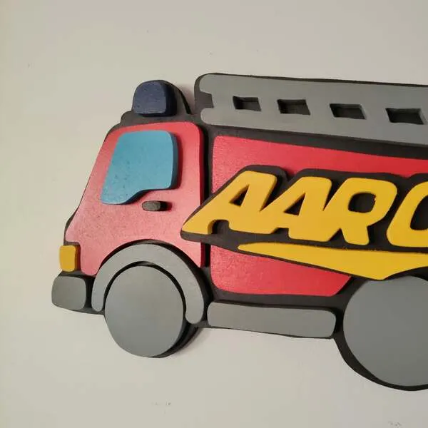 Gros plan sur l'avant d'une plaque de porte camion de pompier rouge en bois, personnalisée avec le prénom Aaron en lettres jaunes et réalisée en relief.